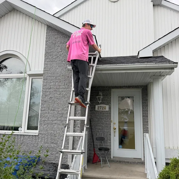 Un technicien Pink Exterior nettoie une fenêtre à l'étage depuis une échelle.