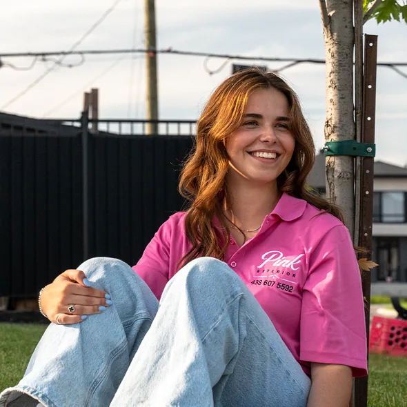 Un membre de l'équipe Pink Exterior en polo rose est assis dans l'herbe.