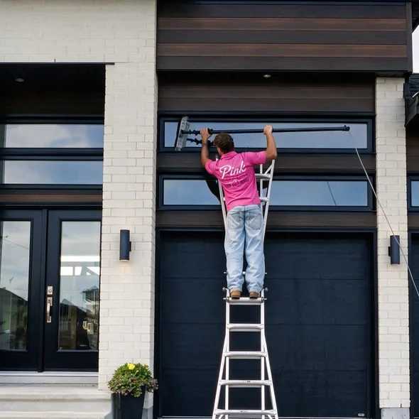 Un technicien nettoie la vitre au-dessus d'une porte de garage depuis un escabeau.
