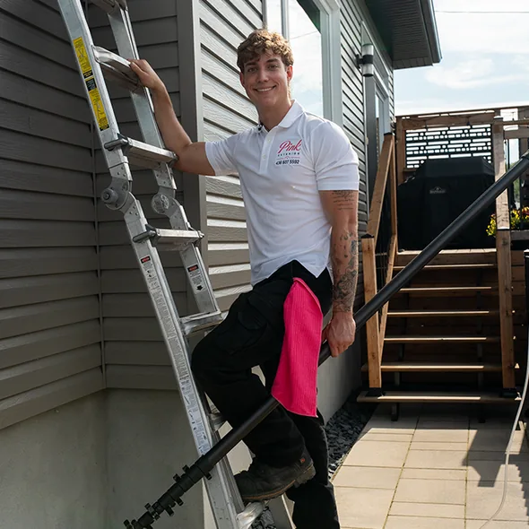 Un technicien Pink Exterior se tient avec une échelle près d'une maison.